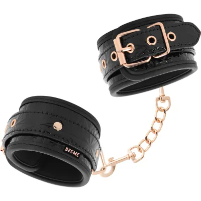 Schwarze Handfesseln mit goldenen Schnallen und Kette, stilvoll und modern gestaltet.