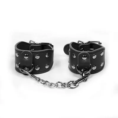 Schwarze Leder-Handfesseln mit Nieten und Kette auf weißem Hintergrund.