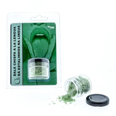 Grünes Knisterpulver in einem Glas, daneben Verpackung mit gezeichneter Zunge und Text auf Spanisch und Portugiesisch.