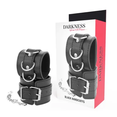 Schwarze Lederhandschellen mit Metallringen und Schnallen, neben einer Verpackung mit der Aufschrift "Darkness".