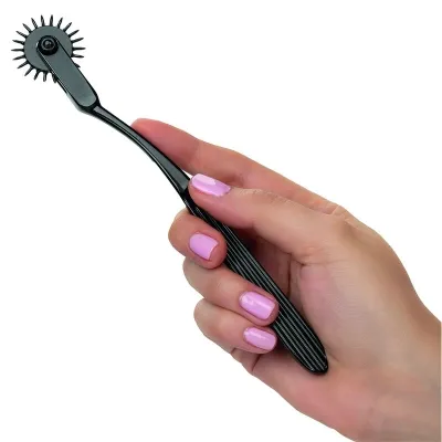 Hand holding a black Wartenberg wheel with pink painted nails.
