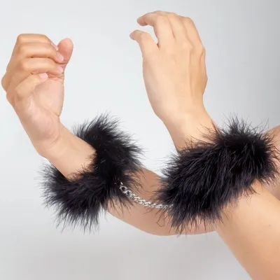 Hände in schwarzen, flauschigen Handschellen mit silberner Kette.