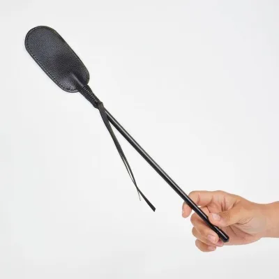 Hand hält eine schwarze Reitgerte mit Lederklatsche vor weißem Hintergrund.