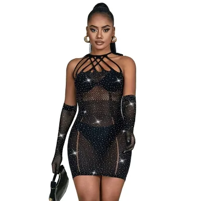 Woman in a black, glittery dress with a net design and matching gloves, holding a small bag.