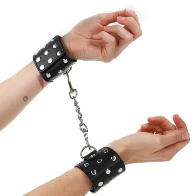 Hände in schwarzen Lederfesseln mit Metallnieten, verbunden durch eine Kette.