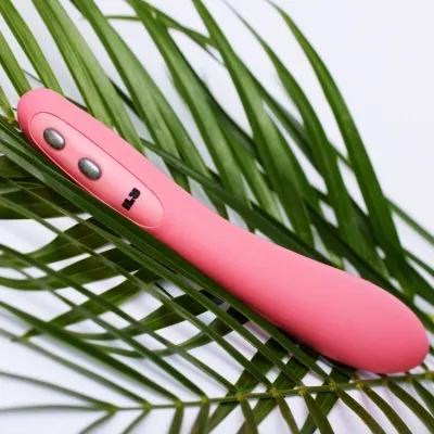 Pink vibrator on green palm leaves, white background.