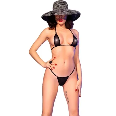 Person in schwarzem Bikini und großem Hut, posiert mit einer Hand auf der Hüfte vor weißem Hintergrund.