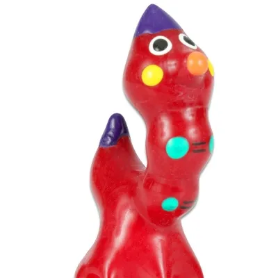Rote, bunte Plastikfigur mit Augen, gelben Wangen und lila Details, die einem fantasievollen Tier ähnelt.