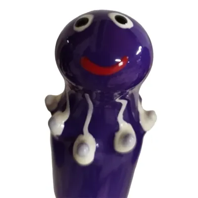 Purple ceramic figurine with large eyes and a red smile, decorated with white dots and lines.