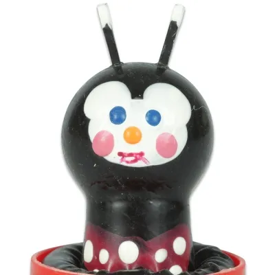 Schwarze Spielzeugfigur mit weißen Punkten, blauen Augen und roten Wangen, auf rotem Sockel.