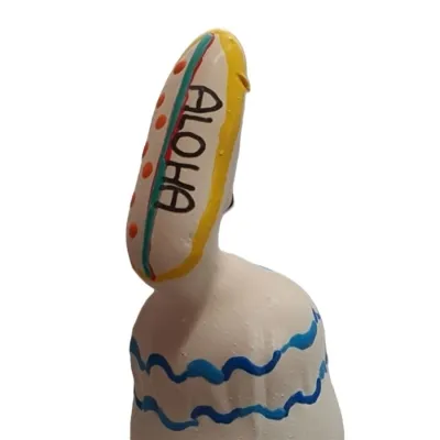 Weiße Figur mit blauen Wellenlinien, gelbem Surfbrett mit "ALOHA" und roten Punkten.