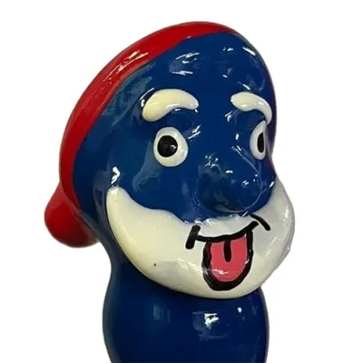 Blaue Cartoonfigur mit roter Mütze, großen Augen und herausgestreckter Zunge.