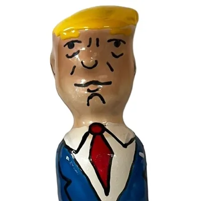 Karikatur einer Person mit gelbem Haar, blauem Anzug und roter Krawatte, aus Keramik geformt.