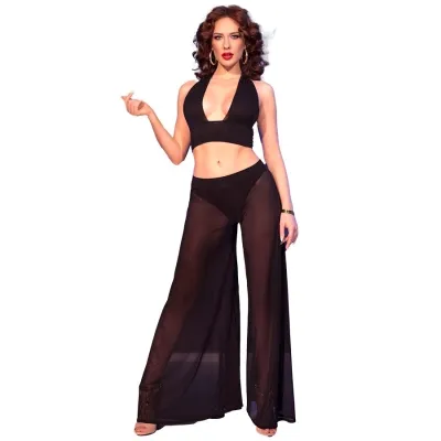 Woman in black, transparent outfit with wide culottes and top, posing in front of a white background.