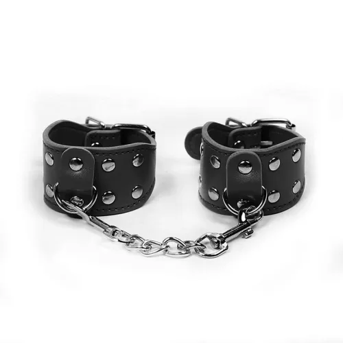 Schwarze Leder-Handfesseln mit Nieten und Kette auf weißem Hintergrund.
