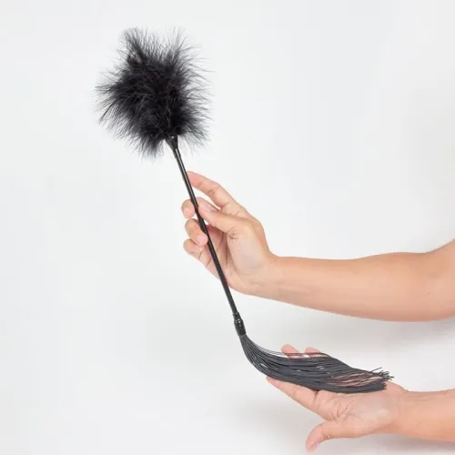 Hand holding a black feather duster with fringes on a white background.