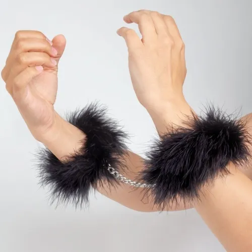 Hände in schwarzen, flauschigen Handschellen mit silberner Kette.