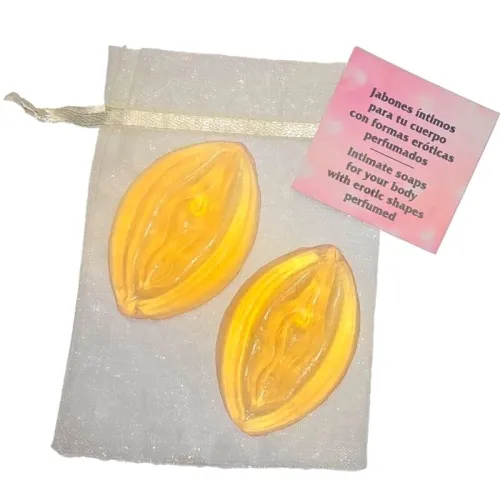 Two yellow soaps in an erotic shape on a white bag with a pink card next to them.