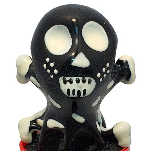 Schwarze Figur mit weißen Augen und Zähnen, die wie ein Skelett aussieht, auf rotem Sockel.