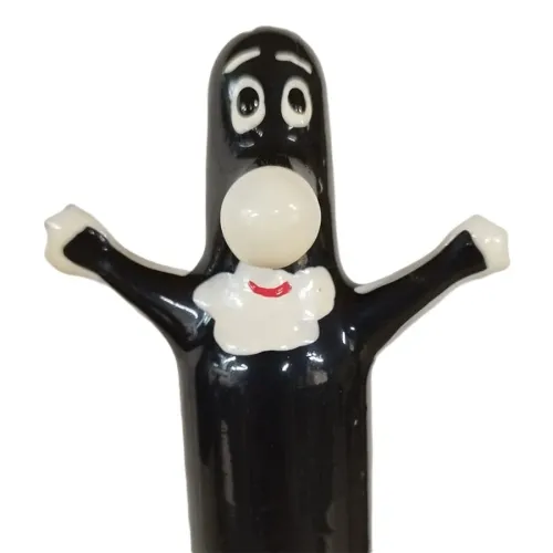 Schwarze Cartoonfigur mit großen Augen, weißem Gesicht und erhobenen Armen, trägt ein weißes Lätzchen mit rotem Lächeln.