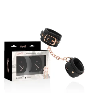 Schwarze vegane Lederhandschellen mit goldenen Details, neben der Verpackung mit Coquette-Logo.