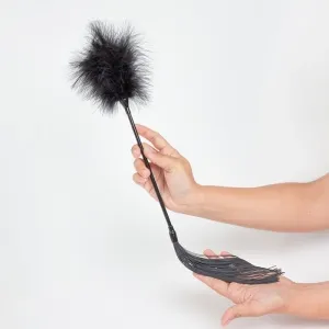 Hand holding a black feather duster with fringes on a white background.