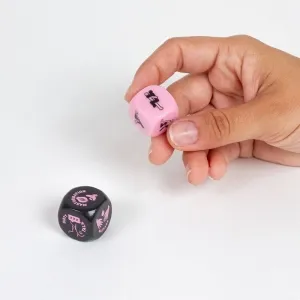 A hand holds a pink cube with symbols, next to it a black cube on a table.