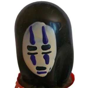 Figur mit weißer Maske und lila Markierungen, schwarzer Umhang, auf rotem Sockel.