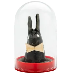 Black rabbit figurine with bow tie under a transparent dome on a red base.